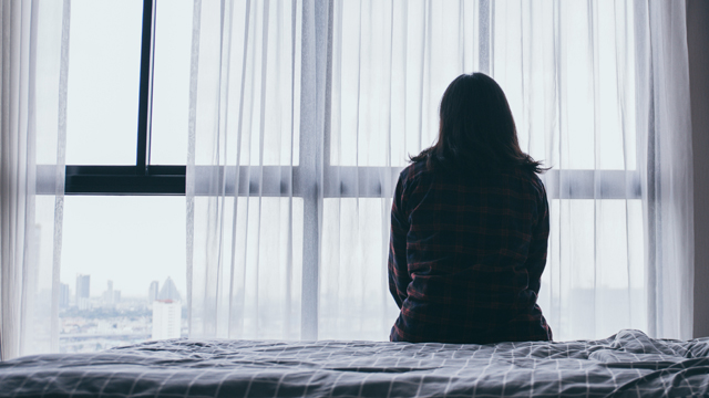 View from behind of a woman sat on a bed looking out of the window