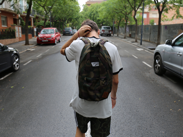 A teenager with a backpack walking down the middle of a road