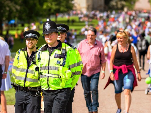 Three police officers walking in the foreground and people in casual wear walking the background on a sunny day
