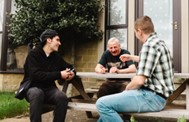 Three men talking whilst sat at a picnic bench