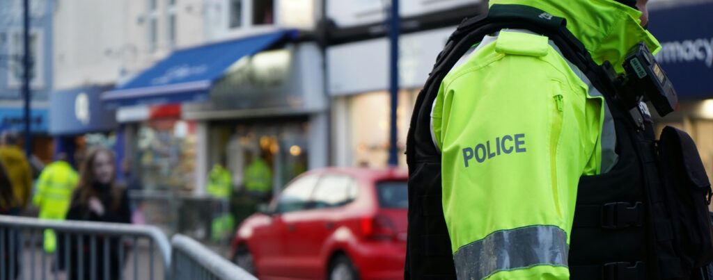 Police officer in a high-vis jacket on a street with shops and pedestrians